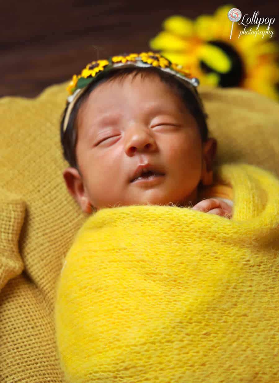 Close-up of a newborn wearing a yellow swaddle and sunflower headband, peacefully asleep in Chennai.