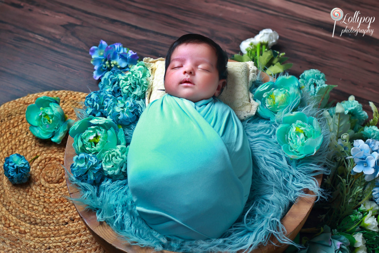 Newborn peacefully wrapped in blue, surrounded by flowers during an elegant newborn photoshoot in Coimbatore.